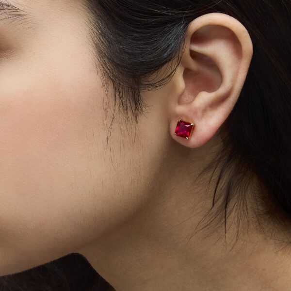 Ruby princess cut stud earrings worn on an ear