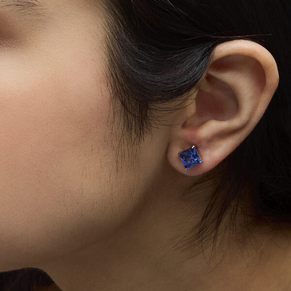 Princess-cut blue sapphire stud earrings worn in a model's ear