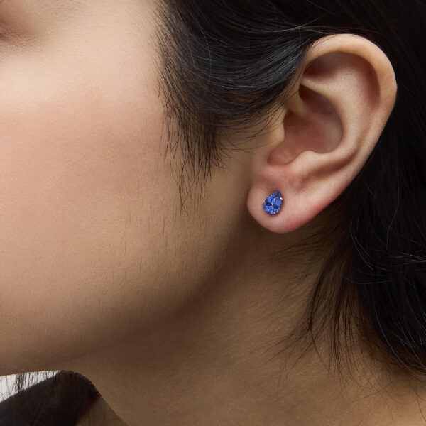 Platinum pear sapphire stud earrings worn in a model's ear