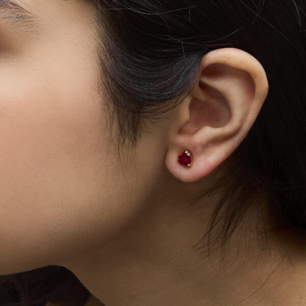 Ruby heart stud earrings shown worn on an ear
