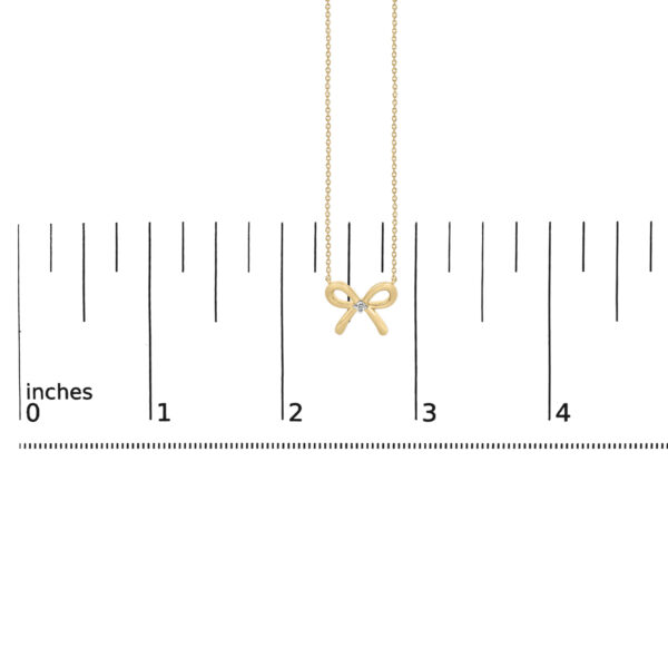 Bow tie pendant necklace shown alongside a scale reference to indicate its size