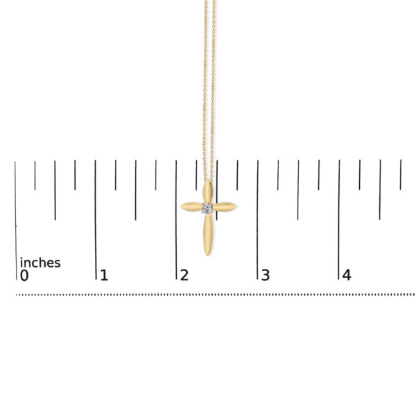 Cross pendant necklace laid flat next to a scale reference to show its size