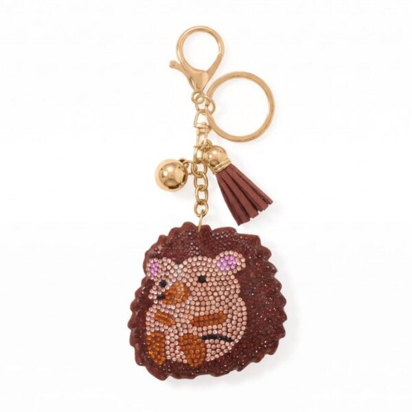 Gold tone hedgehog bag charm covered in crystal accents with a tassel and bell charm attached